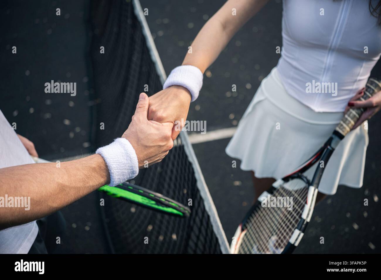 Nahaufnahme von männlichen und weiblichen Tennisspielern, die sich über das Netz die Hand geben und Sportgeist, Respekt und Fair Play nach einem Outdoor-Match zeigen. Stockfoto