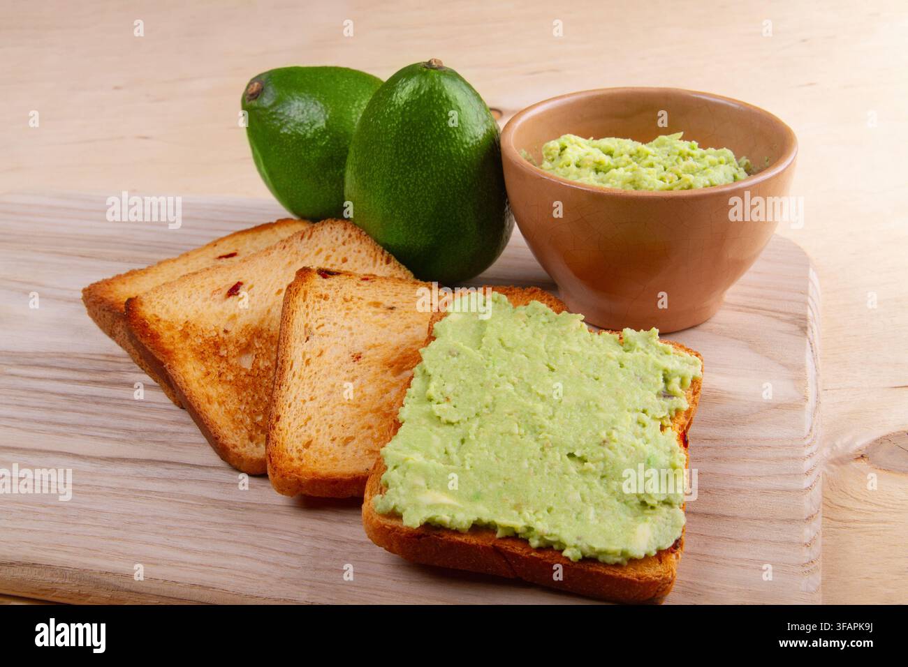 Avocado-Toast auf Vollkornbrot, gehackte Avocado auf heller beiger Holzarbeitsplatte. Gesundes Ernährungs-Konzept Stockfoto