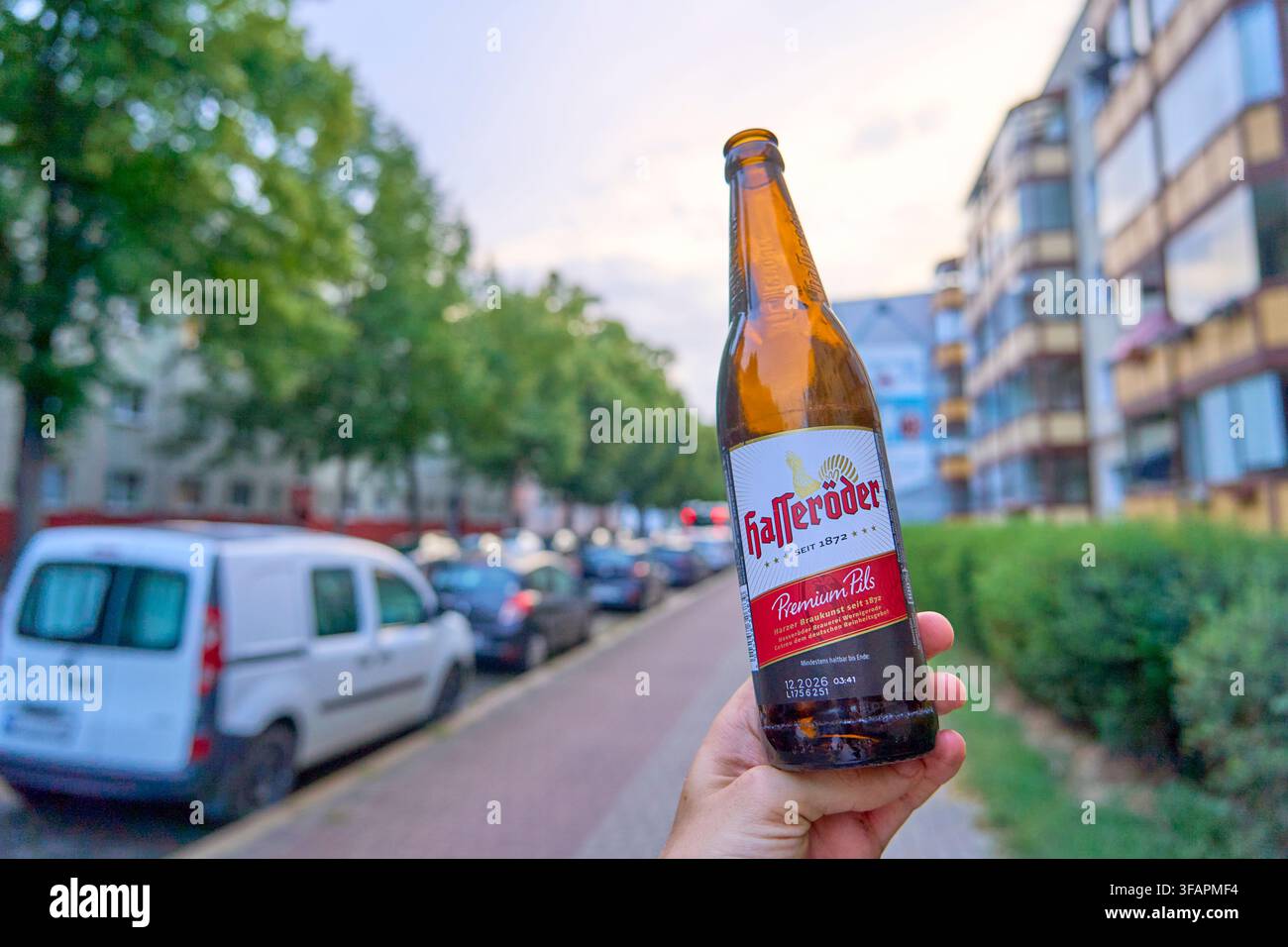 Individuelle Stressbewältigung durch regionale Konsumtion innerhalb rigider urbaner Strukturen, symbolisiert durch eine Hand, die eine offene Flasche Hasseröder-Bier hält, r Stockfoto