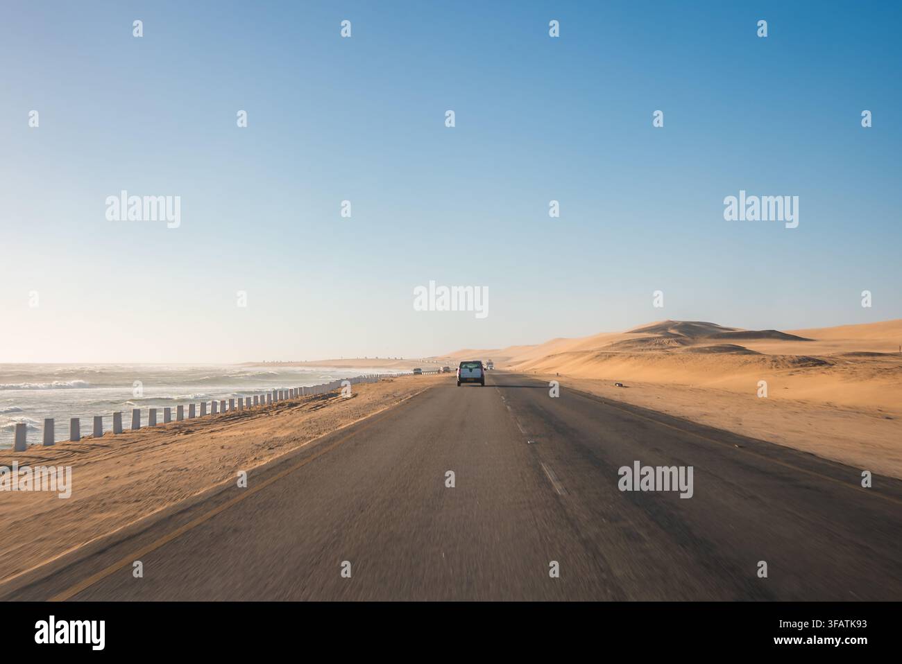 Auto fährt entlang einer Küstenwüstenstraße zwischen Ozean und Dünen in Namibia Stockfoto