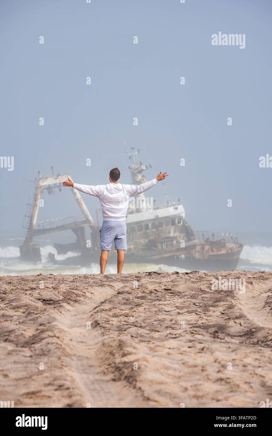 Mann steht am sandigen Ufer und betrachtet das Wrack von Zeila in Namibia Stockfoto