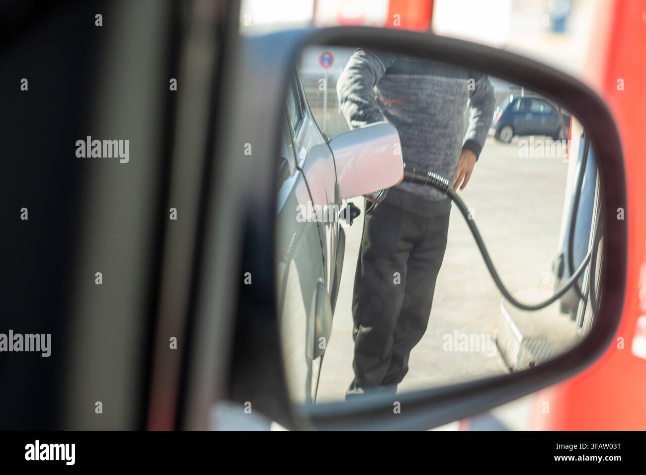 Ein Mann betankt sein Auto an einer Tankstelle. Das Bild ist ein Spiegelbild des Mannes im Spiegel Stockfoto
