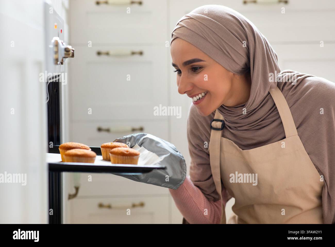 Glücklich Schöne Muslimische Frau In Hijab Backen Muffins In Der Küche Zu Hause Stockfoto