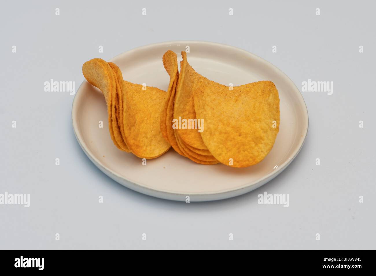 Ein kleiner Stapel Kartoffelchips liegt auf einem Teller vor einem weißen Hintergrund. Stockfoto