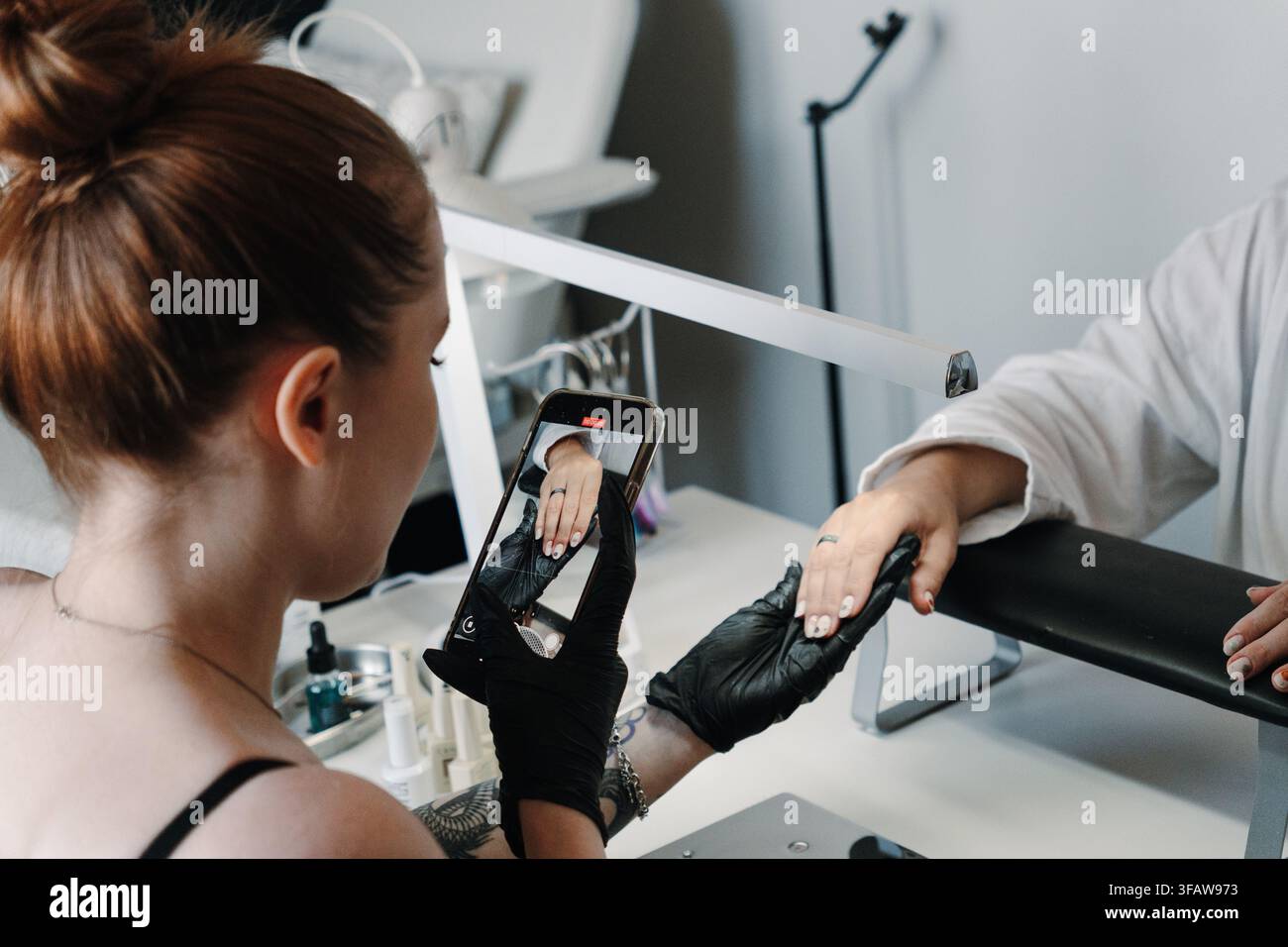Frauen-Nageltechnikerin fotografiert oder filmt eine fertige Maniküre mit einem Smartphone im Salon. Schönheit-Marketingkonzept für Portfolio, Social Media Stockfoto