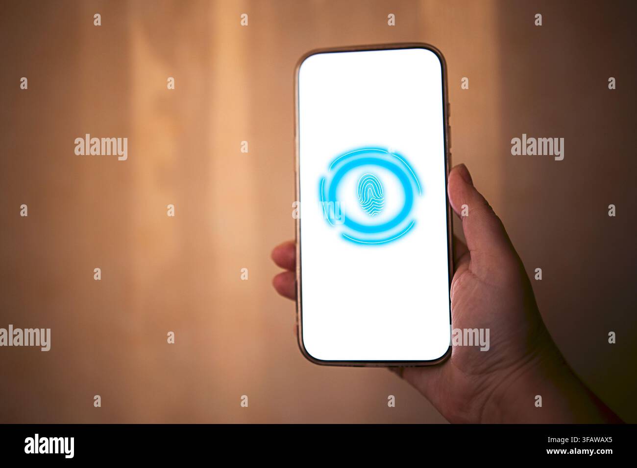 Hand, die ein Smartphone mit einem leeren Bildschirm hält, auf dem ein Fingerabdruck-Symbol zu sehen ist, beleuchtet von weichem Licht vor einem unscharfen Hintergrund Stockfoto