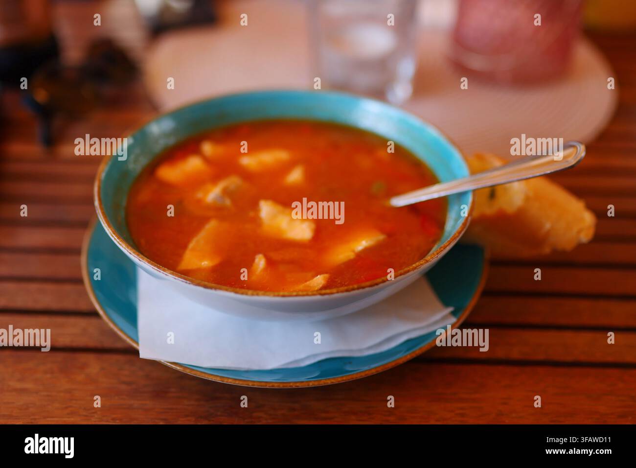 Traditionelle Fischsuppe mit Gemüse serviert in einer Keramikschüssel mit Brot auf einem hölzernen Restauranttisch. Stockfoto