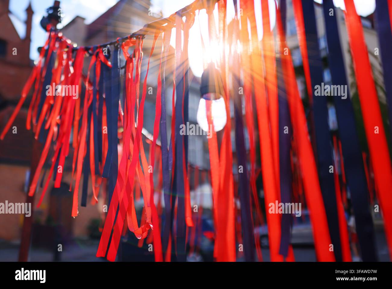 Dekorative rote und schwarze Bänder, die von Sonnenlicht auf einer Stadtstraße beleuchtet werden, abstrakter festlicher Hintergrund mit selektiver Schärfentiefe. Stockfoto