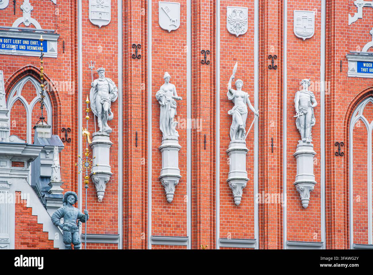 Skulpturale Fassaden-Erbe zeigt sich in einer Reihe von Steinfiguren und heraldischen Plaketten an einem roten Backstein-Denkmal in der Altstadt von Riga als architektonisches Detail Stockfoto