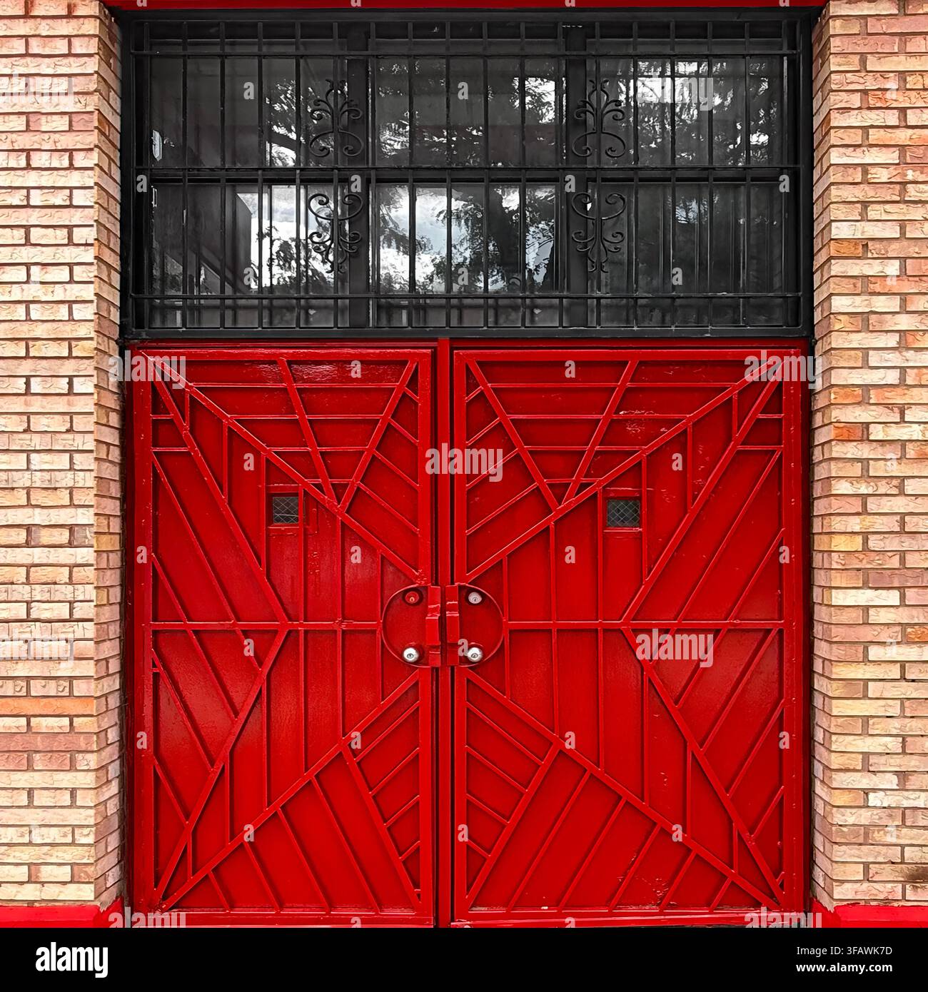 Rote Metall-Doppeltüren mit kräftigem geometrischem Gitterwerk unter einem großen schwarzen Oberlichtfenster an einem Backsteingebäude in Chicago. Stockfoto