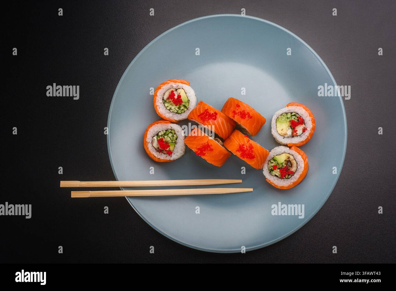 Frisches japanisches Sushi-Set mit Lachs und Frischkäse, serviert auf einem hellblauen Teller mit hölzernen Essstäbchen, Nahaufnahme. Stockfoto