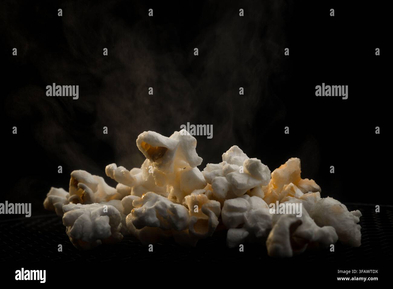 Haufen frisch geplatzten weißen Popcorns mit aromatischem Dampf auf dunklem Hintergrund Stockfoto