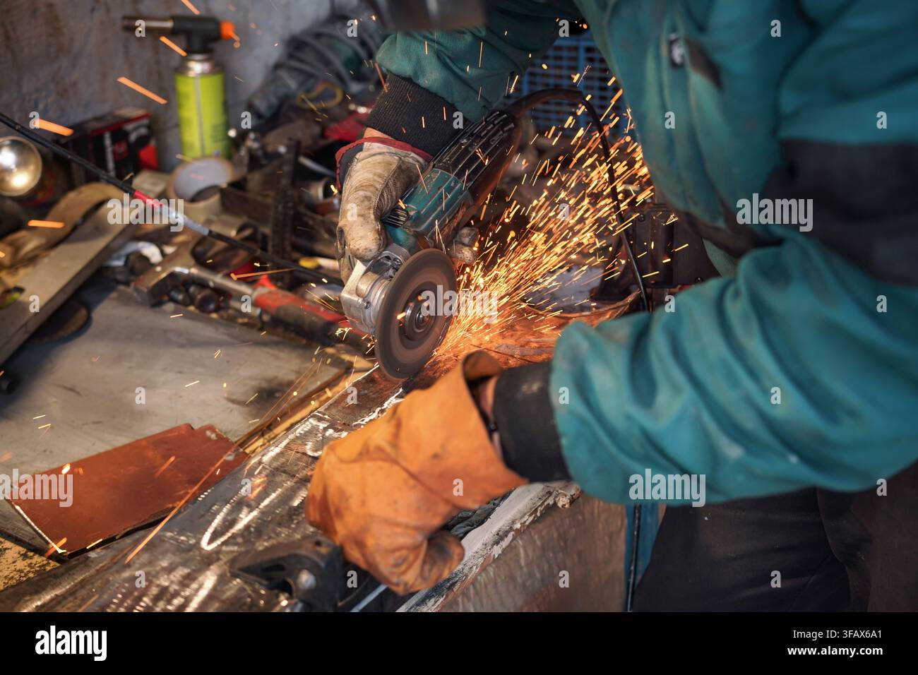 Mann, der in der Werkstatt mit Drehwinkelschleifer arbeitete, Details aus der Nähe, orangefarbene Funken flogen herum Stockfoto
