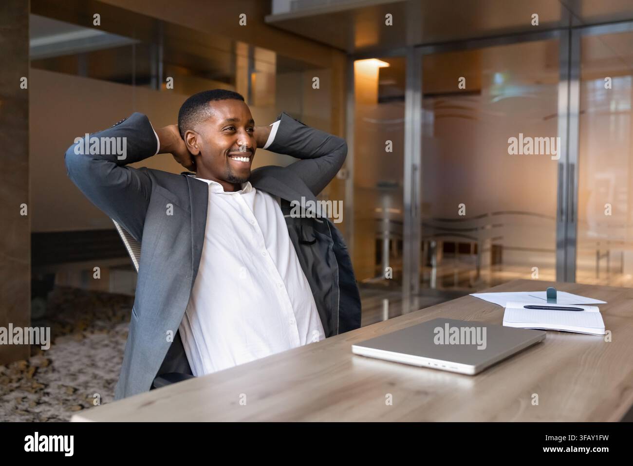 Lächelnder afrikanischer Geschäftsmann am Ende des Arbeitstages, zurückgelehnt im Stuhl Stockfoto