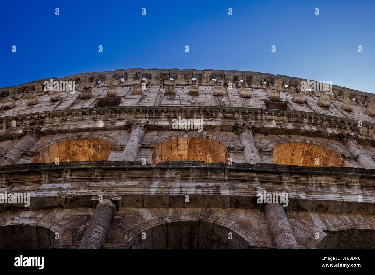 Eine nach oben gerichtete Ansicht der monumentalen Fassade und der gestuften Steinbögen des historischen Kolosseums in Rom, Italien. Stockfoto