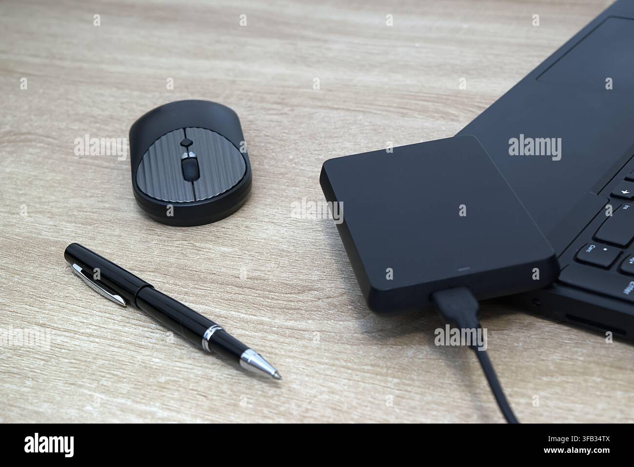 Komposition aus einem Top-Down-Winkel, die eine schwarze tragbare externe Festplatte zeigt, die über USB mit einem Laptop verbunden ist, zusammen mit einer passenden kabellosen Computermaus Stockfoto
