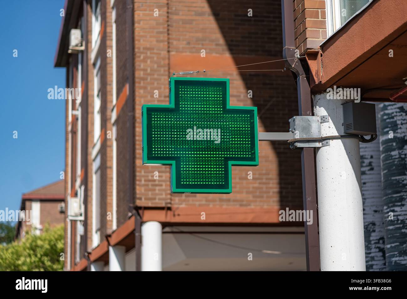 Beleuchtetes grünes Apothekerkreuzschild, das an einem Backsteingebäude unter einem klaren blauen Himmel montiert ist Stockfoto
