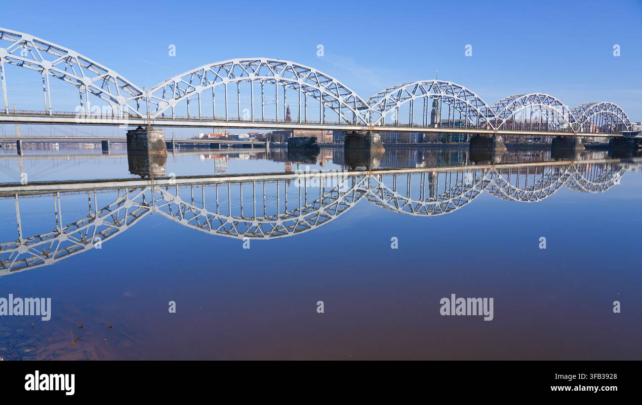 Historische Eisenbahnbrücke, die sich im ruhigen Wasser der Daugava in Riga, Lettland, spiegelt Stockfoto