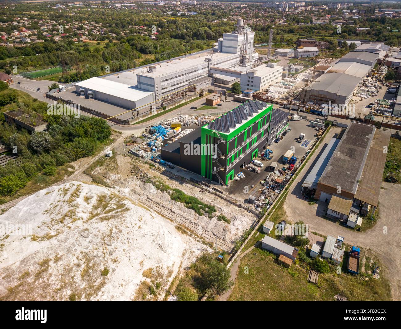 Hochwinkel-Drohnenaufnahme zeigt moderne grüne Recyclinganlage mit Generationselementen auf dem Dach neben großem Sortierbereich und Industriegebäude Stockfoto