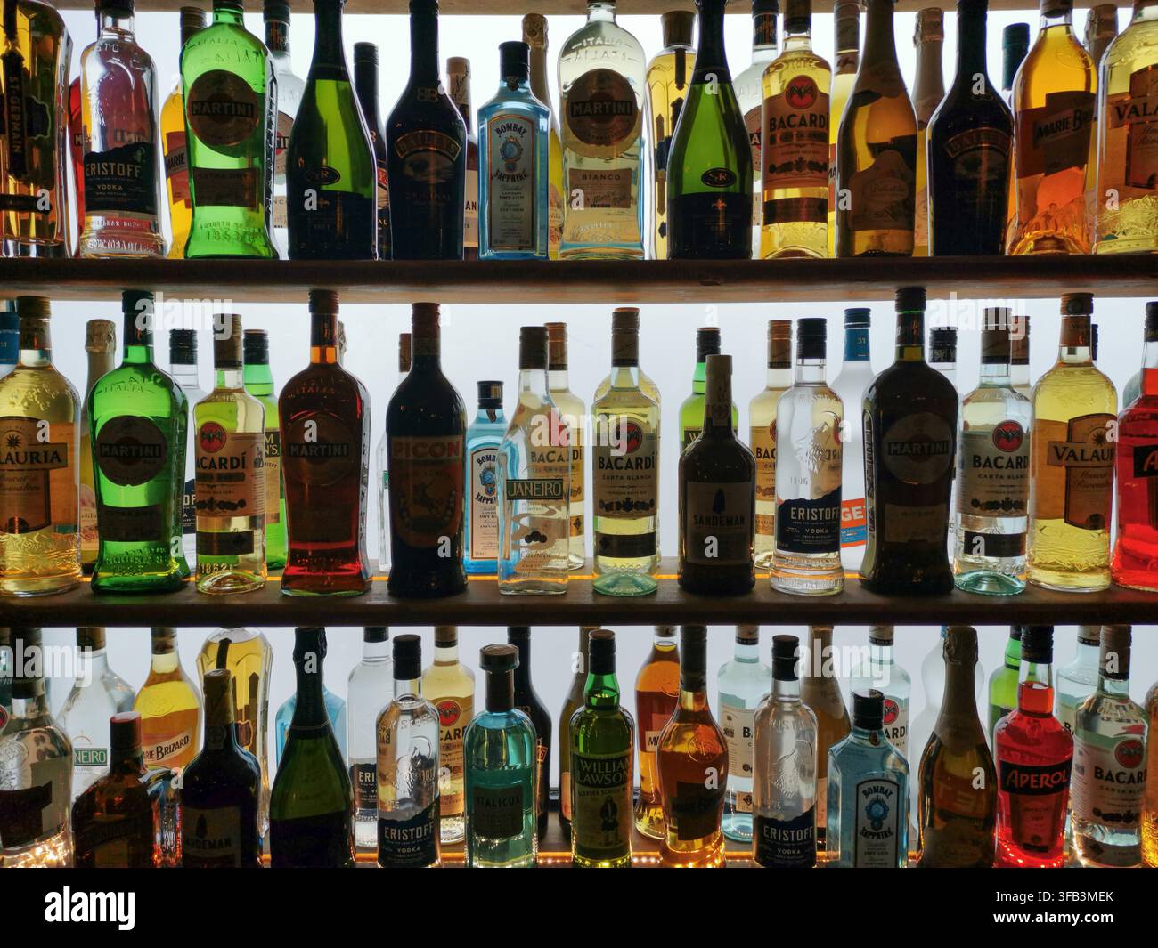 Eine breite Auswahl an Likör- und Spirituosenflaschen säumt drei helle, gut bestückte Regale und schafft eine farbenfrohe Präsentation von alkoholischen Getränken, bereit für Stockfoto