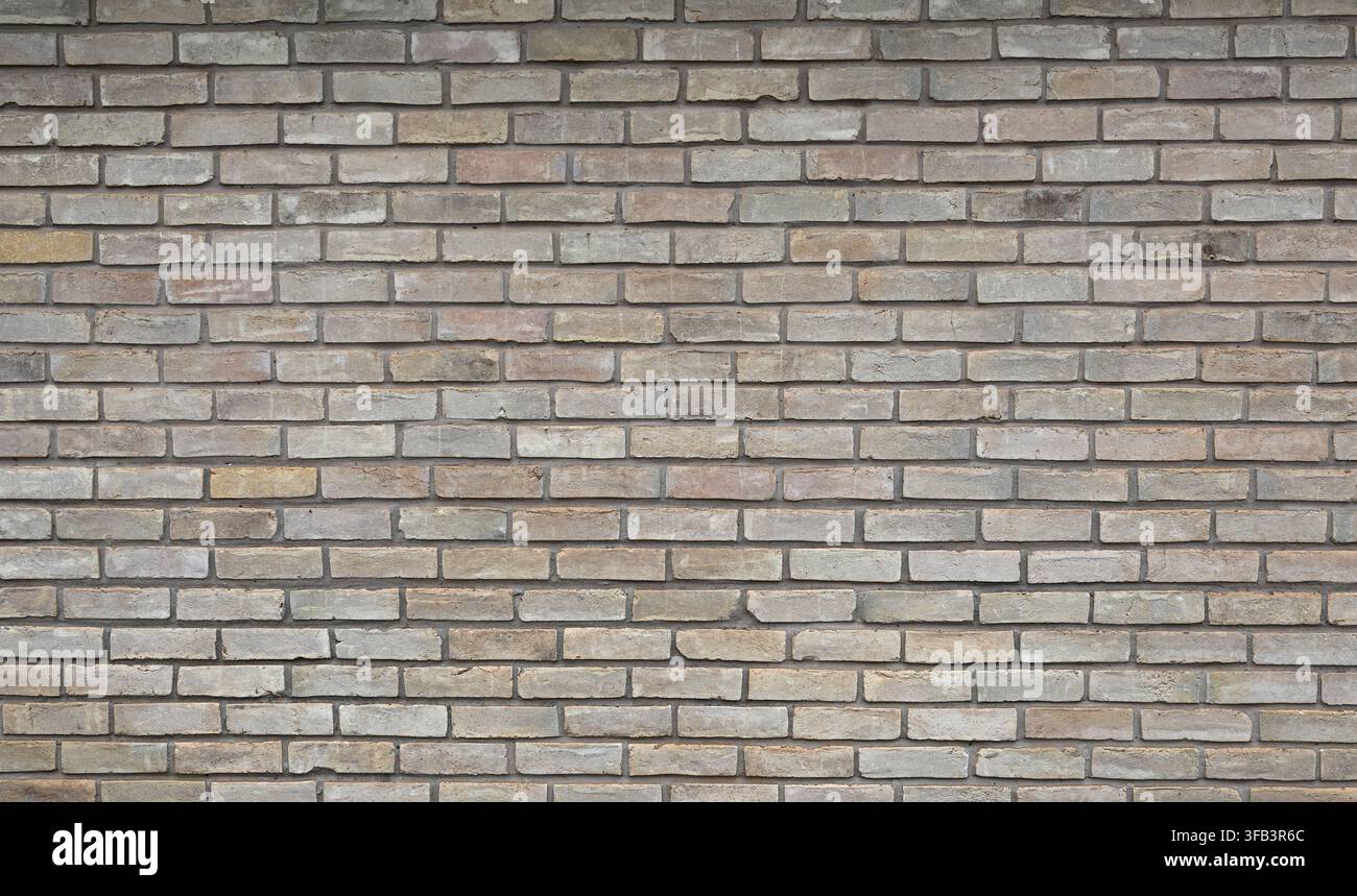 Horizontale Ansicht einer mehrfarbigen braunen Ziegel- und Mörtelwandoberfläche mit porösen, unebenen Ziegeln, glatten Oberflächen und einigen mit dunklen Flecken Stockfoto