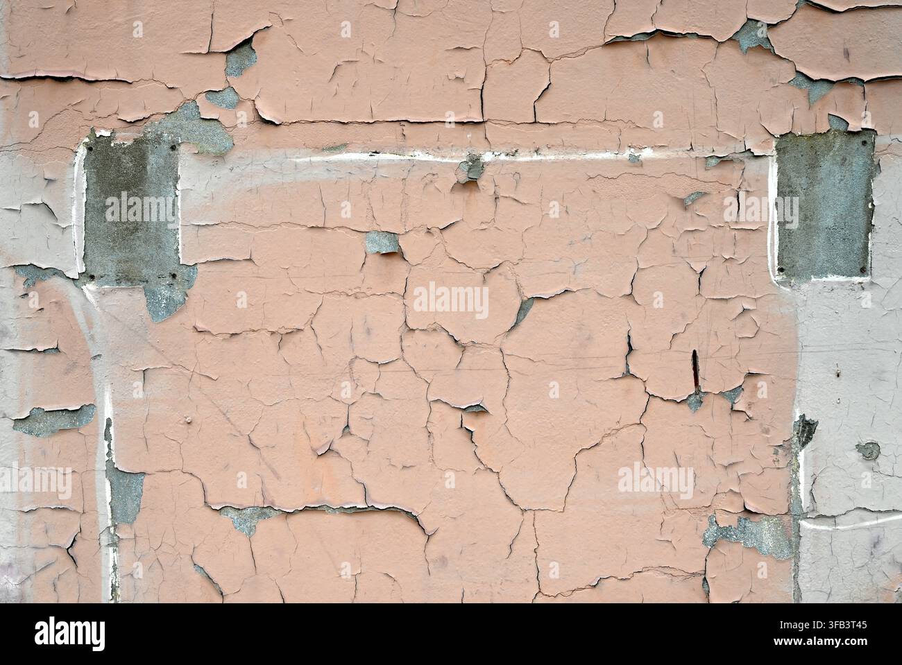 Horizontale Ansicht einer verwitterten, hellbraun gestrichenen Wandfläche mit rissiger, abblätternder Farbe, zwei rechteckigen Betonflecken, hellgrau gestrichener Bereich Stockfoto