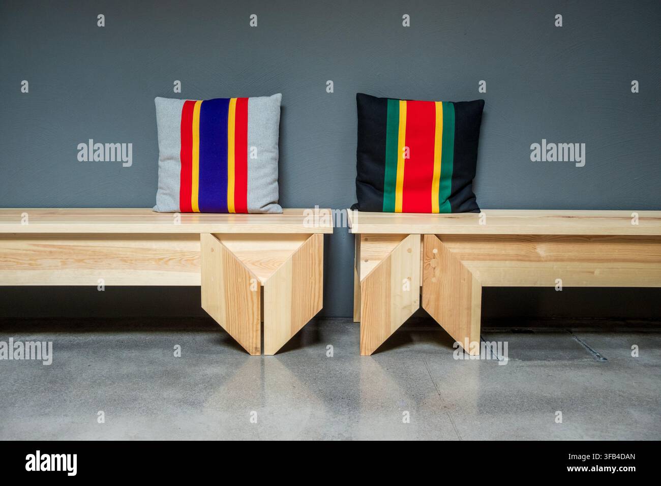 Abstrakte Innenraumkomposition mit zwei Holzbanken und zwei farbenfrohen Kissen Stockfoto