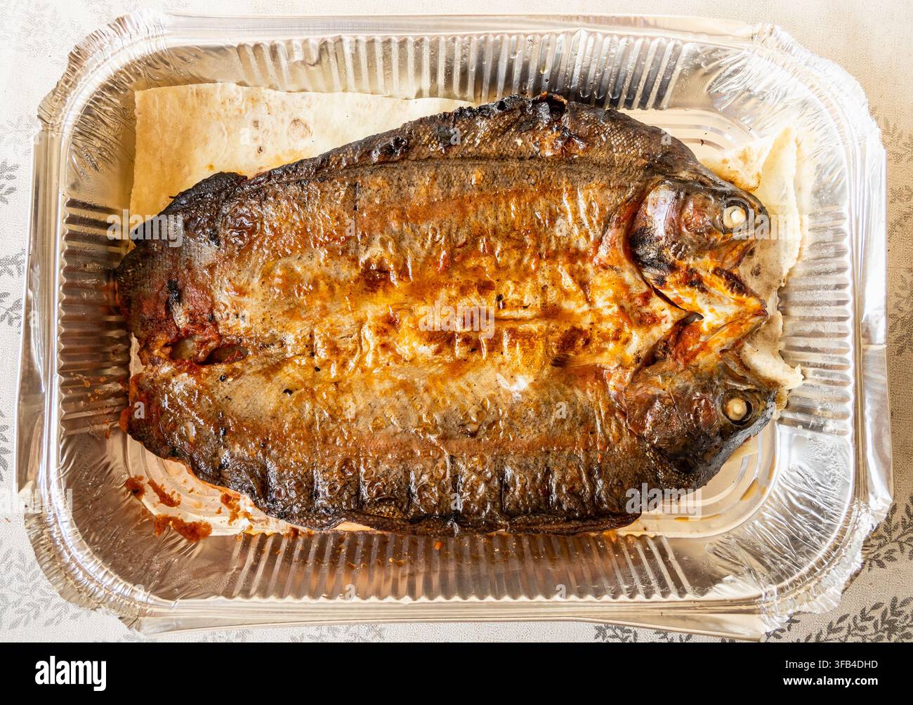 Oberansicht von gegrilltem armenischem Flussforellenfisch in einer Folienpackung auf dem Küchentisch Stockfoto