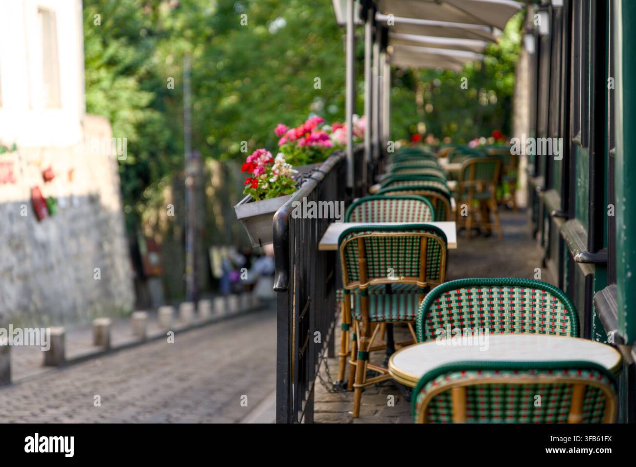 Grüne und rote Korb-Bistrostühle mit runden weißen Tischen und blühenden Pflanzen auf einer schattigen Terrasse in Montmartre, Paris, Frankreich. Stockfoto