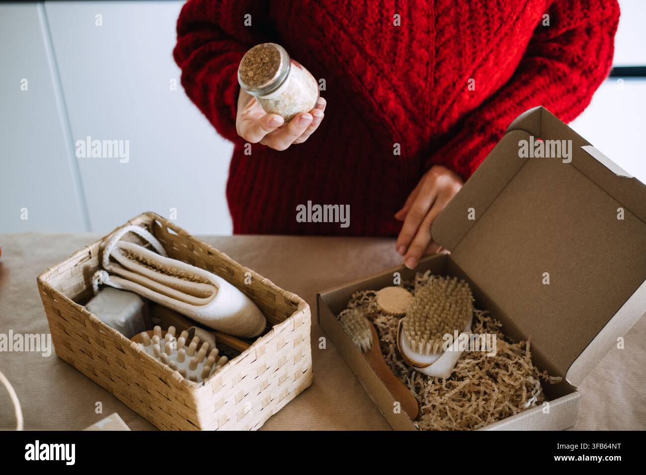 Frau hält Glas mit Badesalz über offene Kraftbox mit Bürsten und Papierfüllung. Qualitätskontrolle handgefertigter Produkte, Überprüfung des Produkts vor dem Versand Stockfoto
