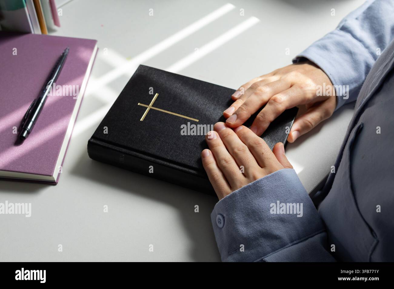 Frau hält die Heilige Bibel im Sonnenlicht während einer ruhigen christlichen Andacht Stockfoto