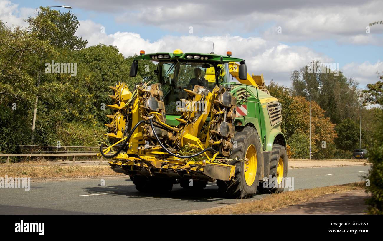 Milton Keynes, UK - 22. August 2026: John Deere 8600i selbstfahrende Futtererntemaschine, ausgestattet mit einem gefalteten gelben Drehmaisschneider, fährt auf Stockfoto