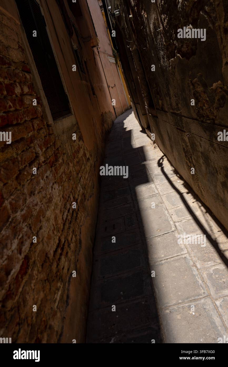 Venedig, Italien - 20. Juni 2026: Atmosphärische vertikale Ansicht einer extrem engen Kopfsteinpflastergasse, flankiert von texturierten Ziegel- und Stuckfassaden. Scharf Stockfoto