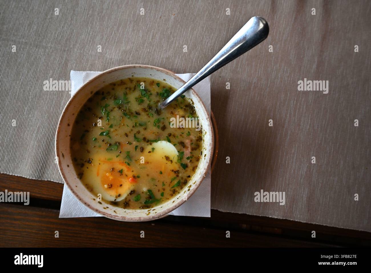 Herzhafte Żurek-Suppe mit gekochtem Ei in einer rustikalen Schüssel mit Löffel auf einem Tischserviette. Stockfoto