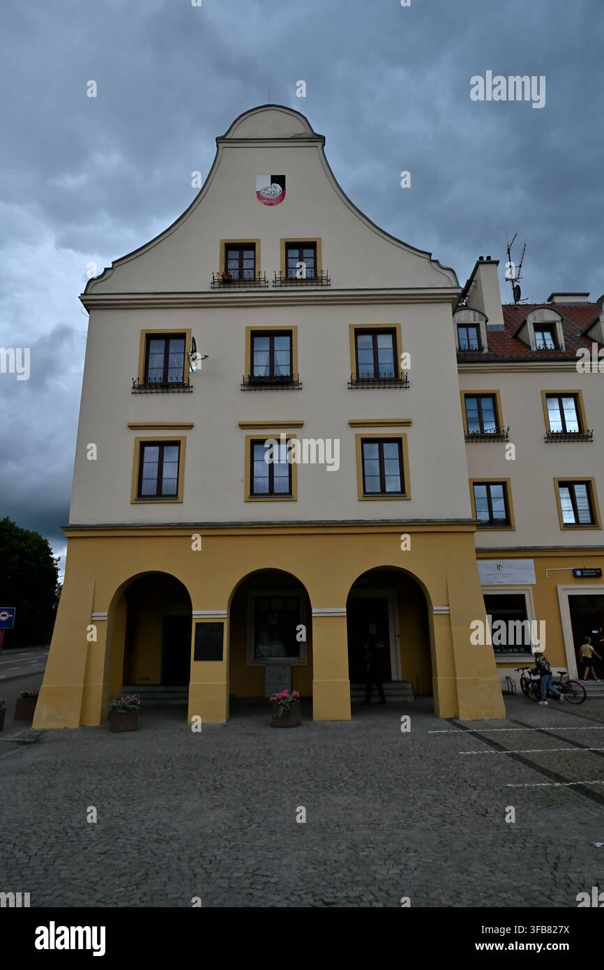 Historische gelbe Gebäudefassade mit gewölbtem Eingang und Giebeldach unter stürmischen Wolken – die Stadt Pisz. Stockfoto