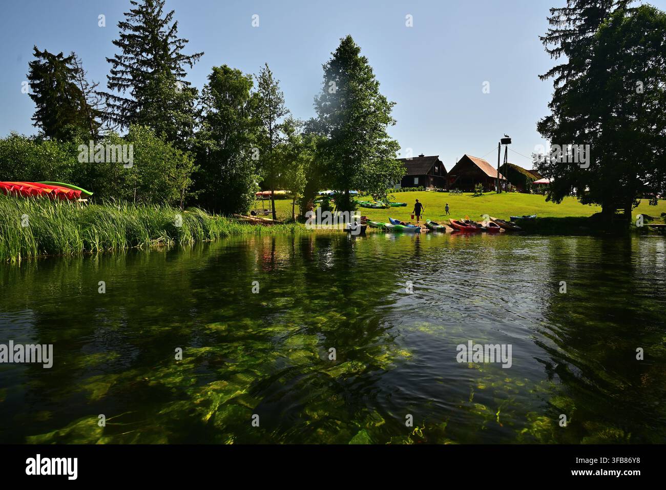 Sommer-Kajakfahrt auf einem sauberen Fluss - Kajakmarina mit Häusern, Bäumen, grüner Wiese und Erholung für Familien - Kajakfahrt auf der Krutynia R Stockfoto