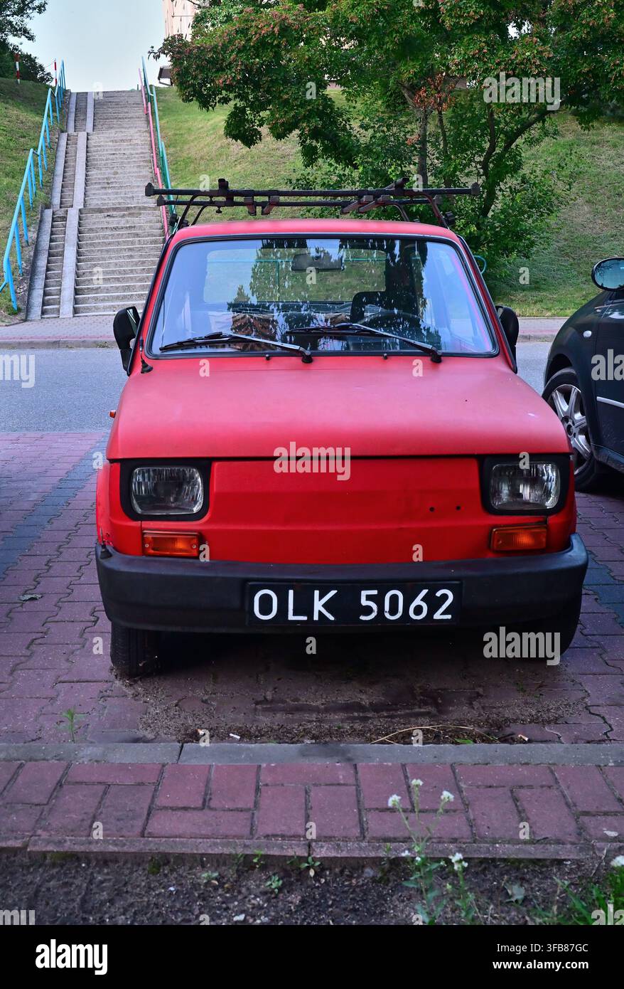 Ein rotes kompaktes Mini-Vintage-Auto, ein Polski Fiat 126p, steht auf der Straße mit einem Dachträger und einem abgenutzten Nummernschild. Stockfoto