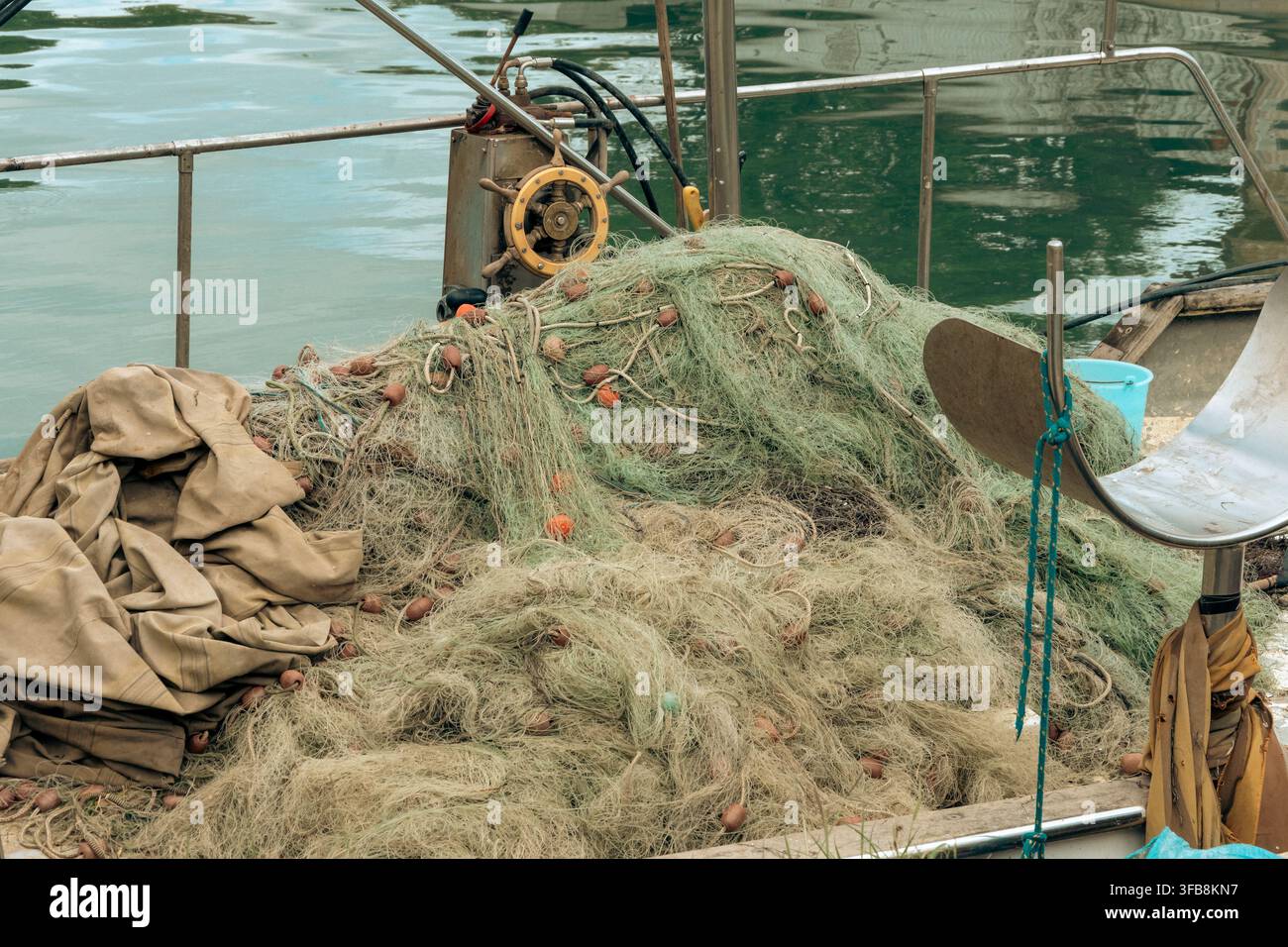 Ein großer Haufen Fischernetze ruht auf einem Bootdeck neben ruhigem grünem Wasser. Stockfoto