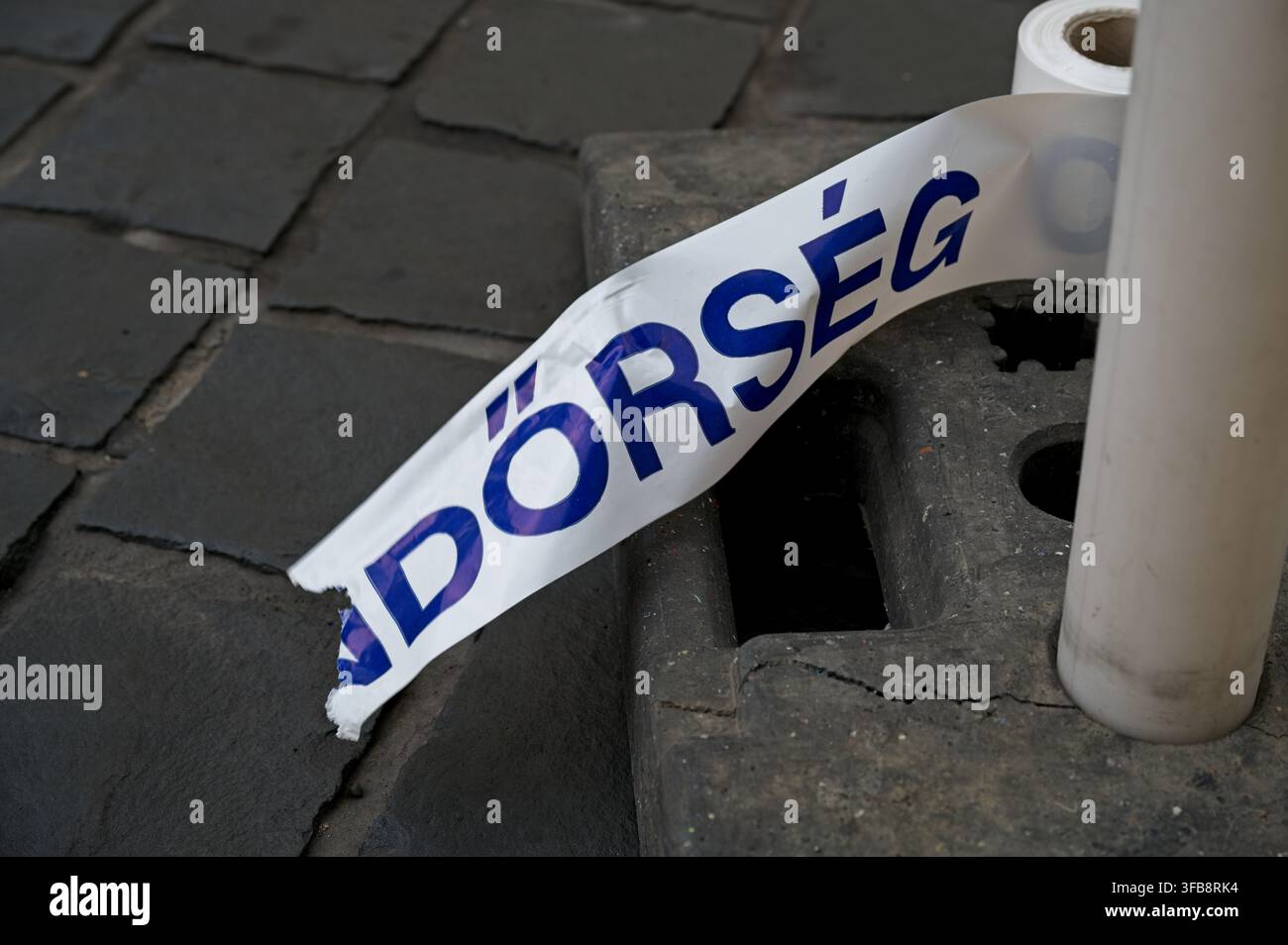 Zerrissenes ungarisches Polizeisiegel mit Text (REN)DORSEG liegt auf dem Boden nahe der Basis eines Barrierepfostens auf einer Kopfsteinpflasterstraße. Stockfoto