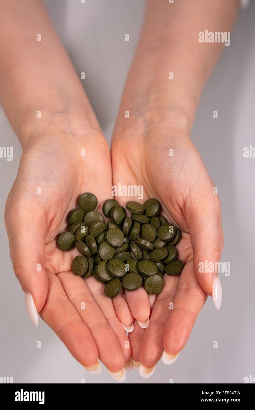 Frau hält grüne Nahrungsergänzungsmittel-Tabletten in den Händen Stockfoto