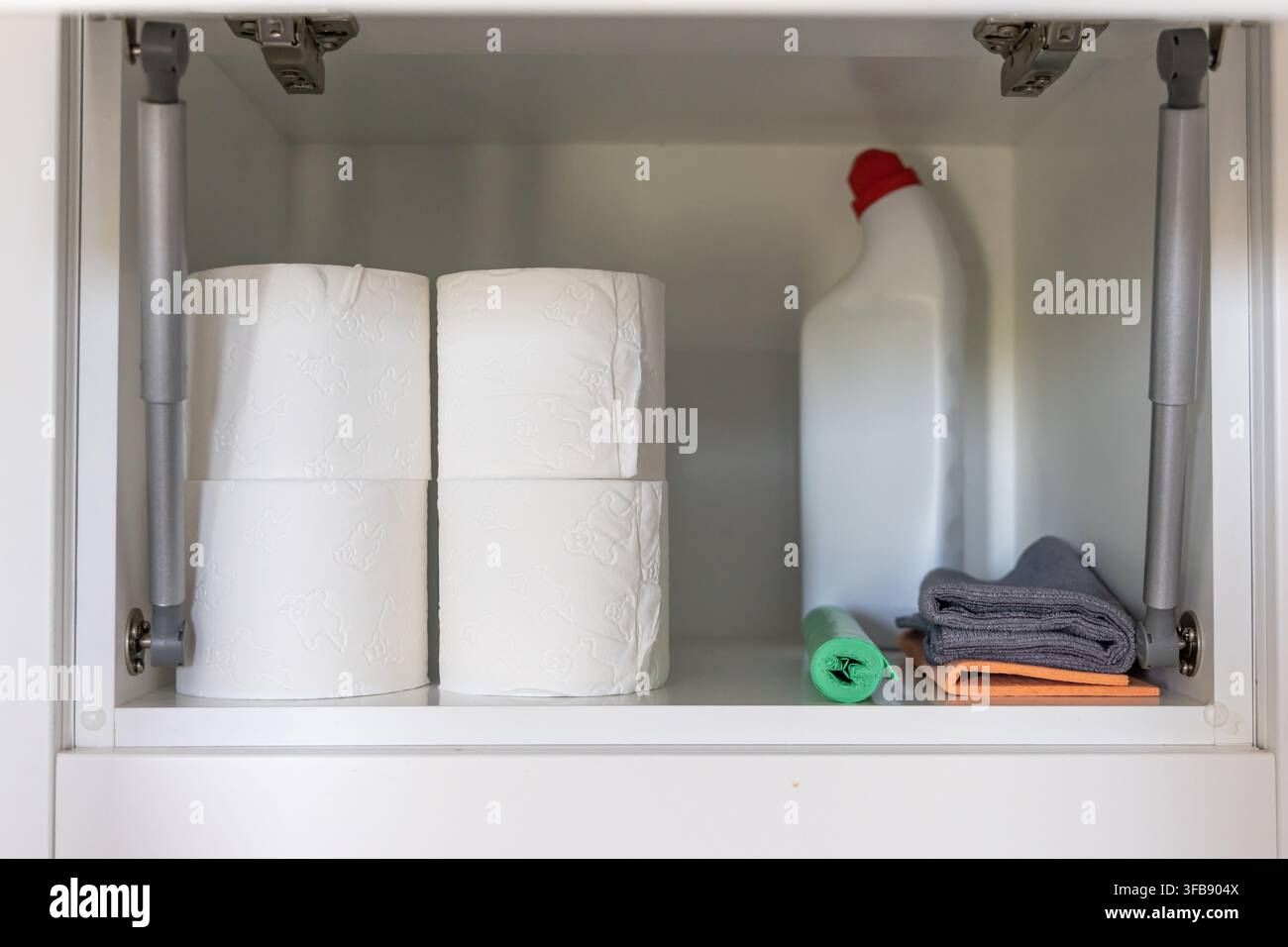 Ein weißes Schrankinnerfach enthält wichtige Haushaltsgegenstände wie Toilettenpapierrollen, eine Reinigungsmittelflasche und gefaltete Tücher für Ordnung Stockfoto