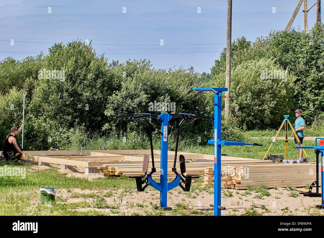 Vermessungstechniker bedient optisches Instrument auf Stativ und koordiniert mit einem Kollegen, der eine Libelle hält, um präzise Messungen auf der Baustelle sicherzustellen. Stockfoto
