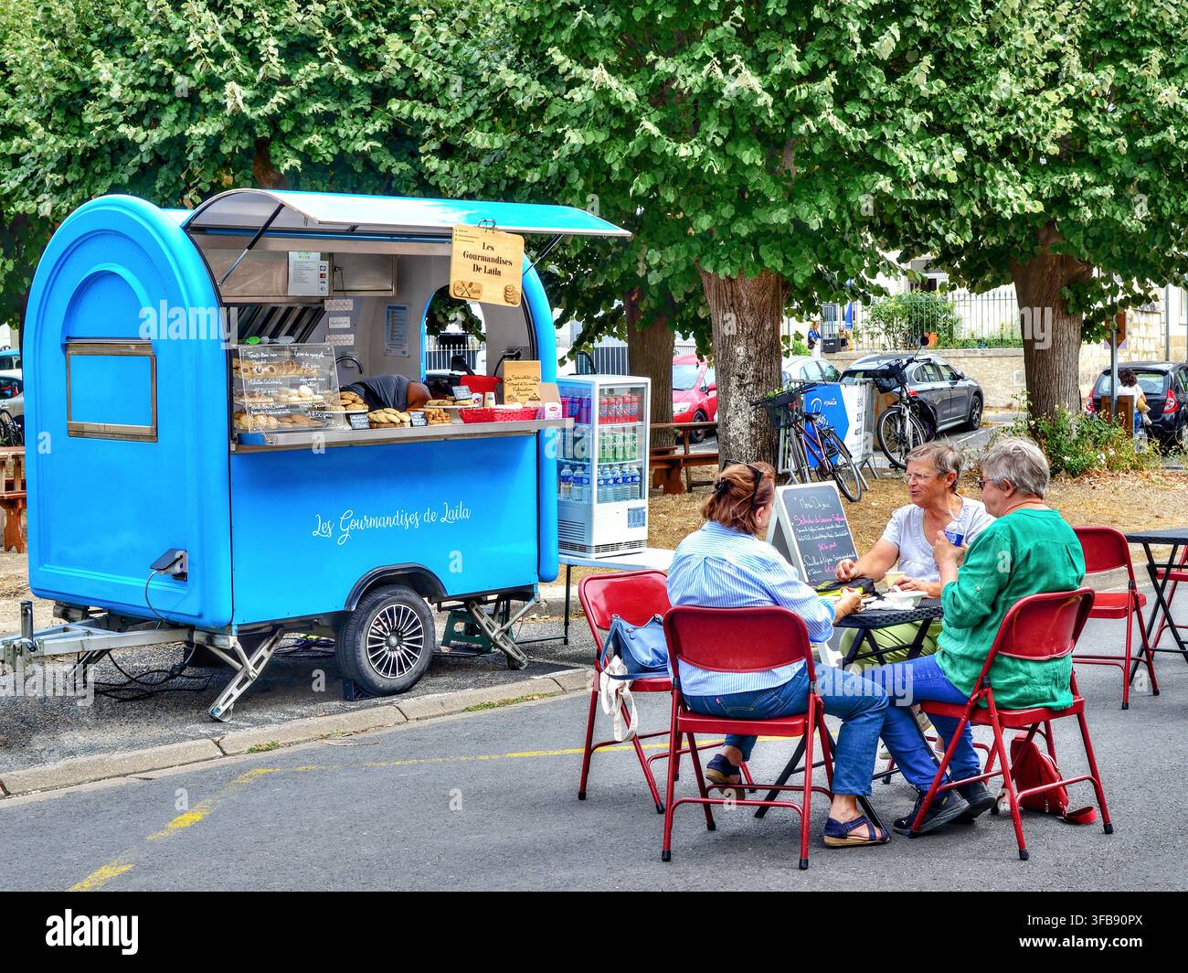 Mobiler Kaffee- und Imbisswagen, der auf dem Stadtplatz geparkt ist, mit Menschen an Stühlen und Tischen - Beaulieu-lès-Loches, Indre-et-Loire (37), Frankreich. Stockfoto