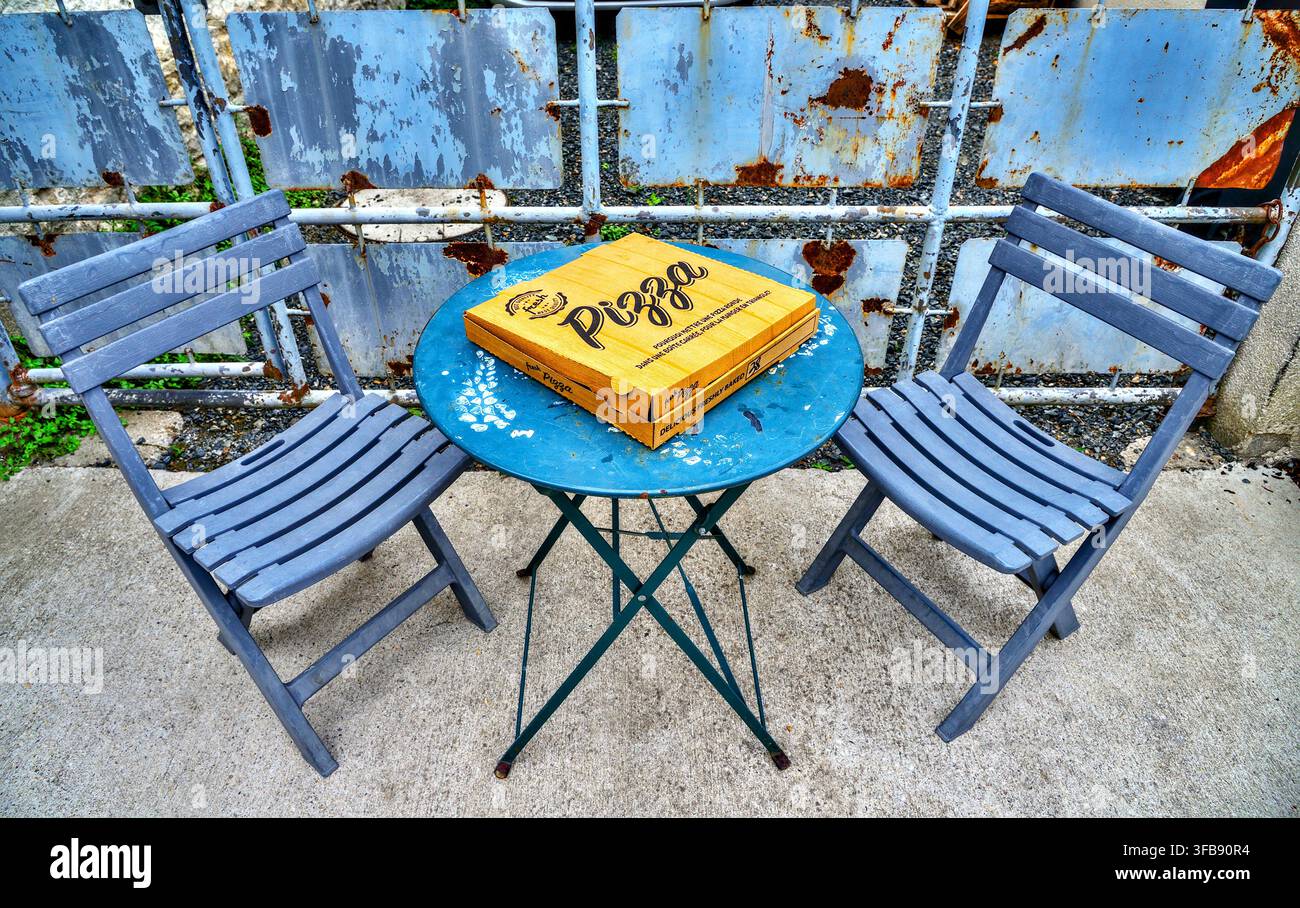 Pizzaschachtel auf blauem Metalltisch und hölzernen Klappstühlen - Beaulieu-lès-Loches (37), Frankreich. Stockfoto