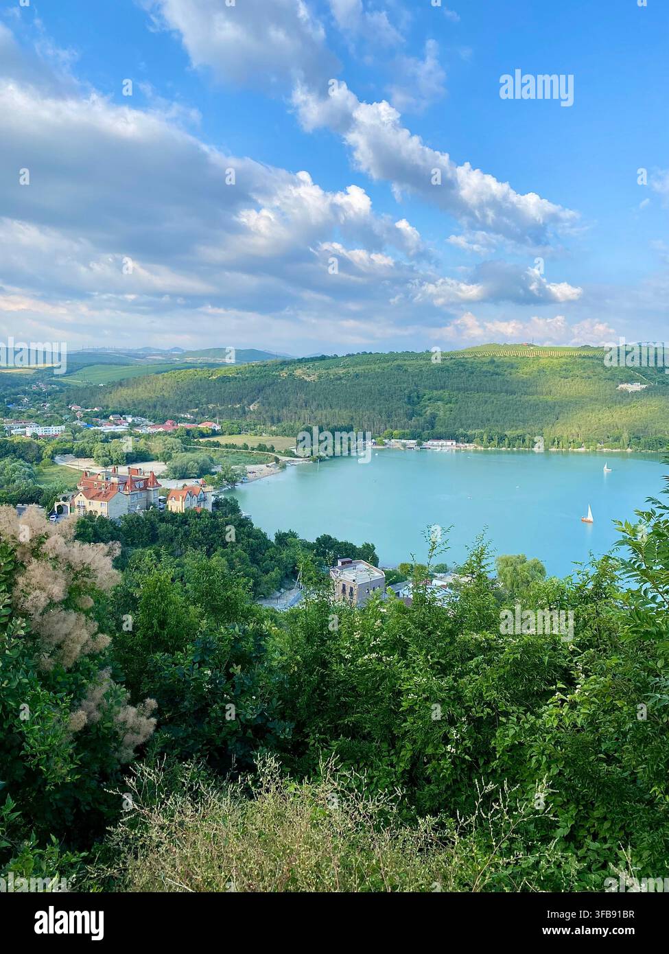 Scenischer türkiser See, umgeben von grünen Hügeln unter dramatischen Sommerwolken - Smartphone-aufgenommenes Stockfoto