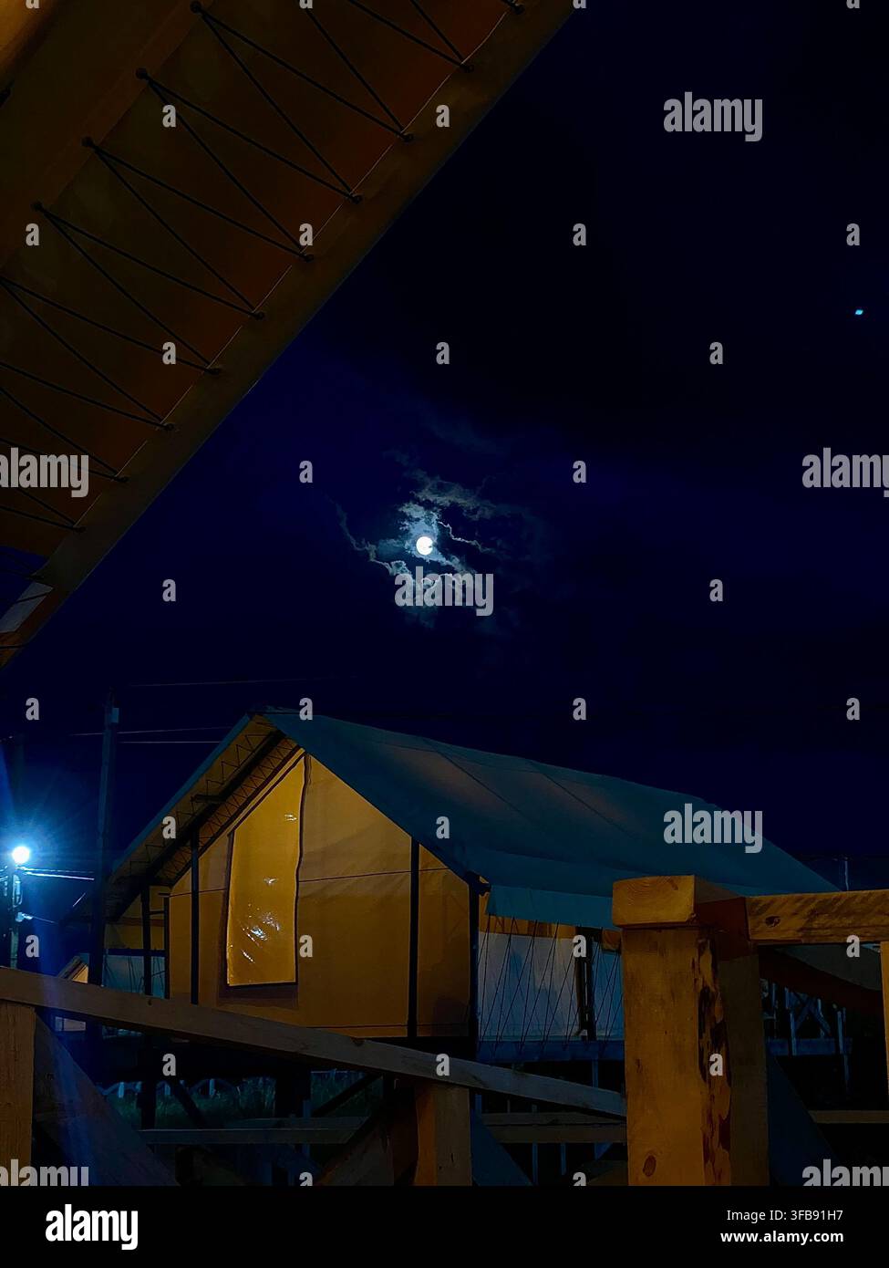 Zelt-Campingzelte aus Canvas, die unter mondbeschienenen Wolken in einer dunklen Sommernacht beleuchtet sind Stockfoto