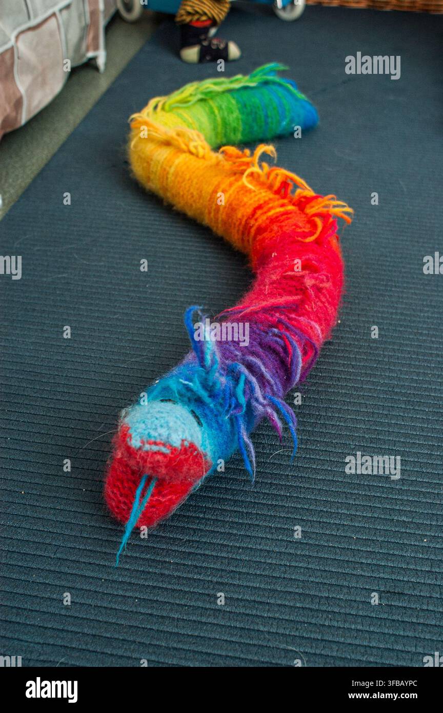 Regenbogenfarbenes gestricktes Spielzeugschlange auf Teppich Stockfoto
