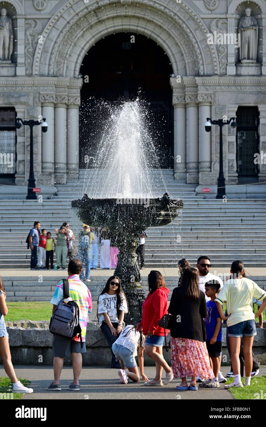 Touristen posieren am Wasserbrunnen vor dem großen steinernen Eingangsbogen des Parlamentsgebäudes von British Columbia in Victoria, Kanada. Stockfoto