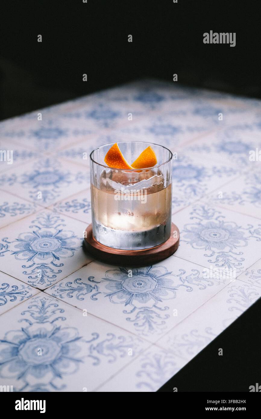 Whisky-Cocktail mit Orangenschale und klarem Eis in einem Rocks-Glas auf blau gemusterten Fliesen, stimmungsvolle Craft-Cocktail-Fotografie Stockfoto