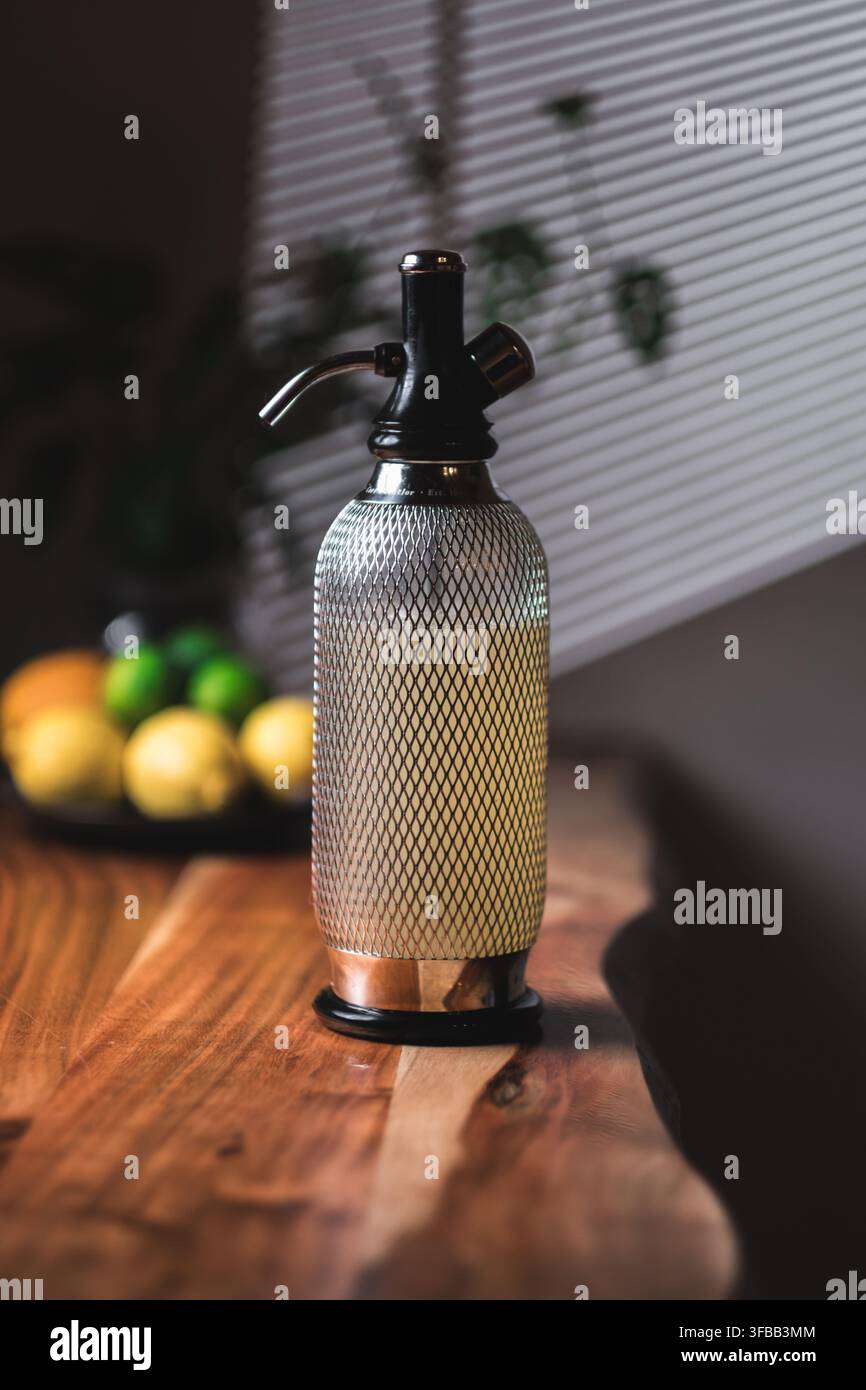 Vintage-Soda-Siphon-Seltersflasche auf einer lebenden Kante Holzbar mit frischen Zitronen und Limetten in einer hellen Küche, Heimbar-Ausrüstung Stockfoto